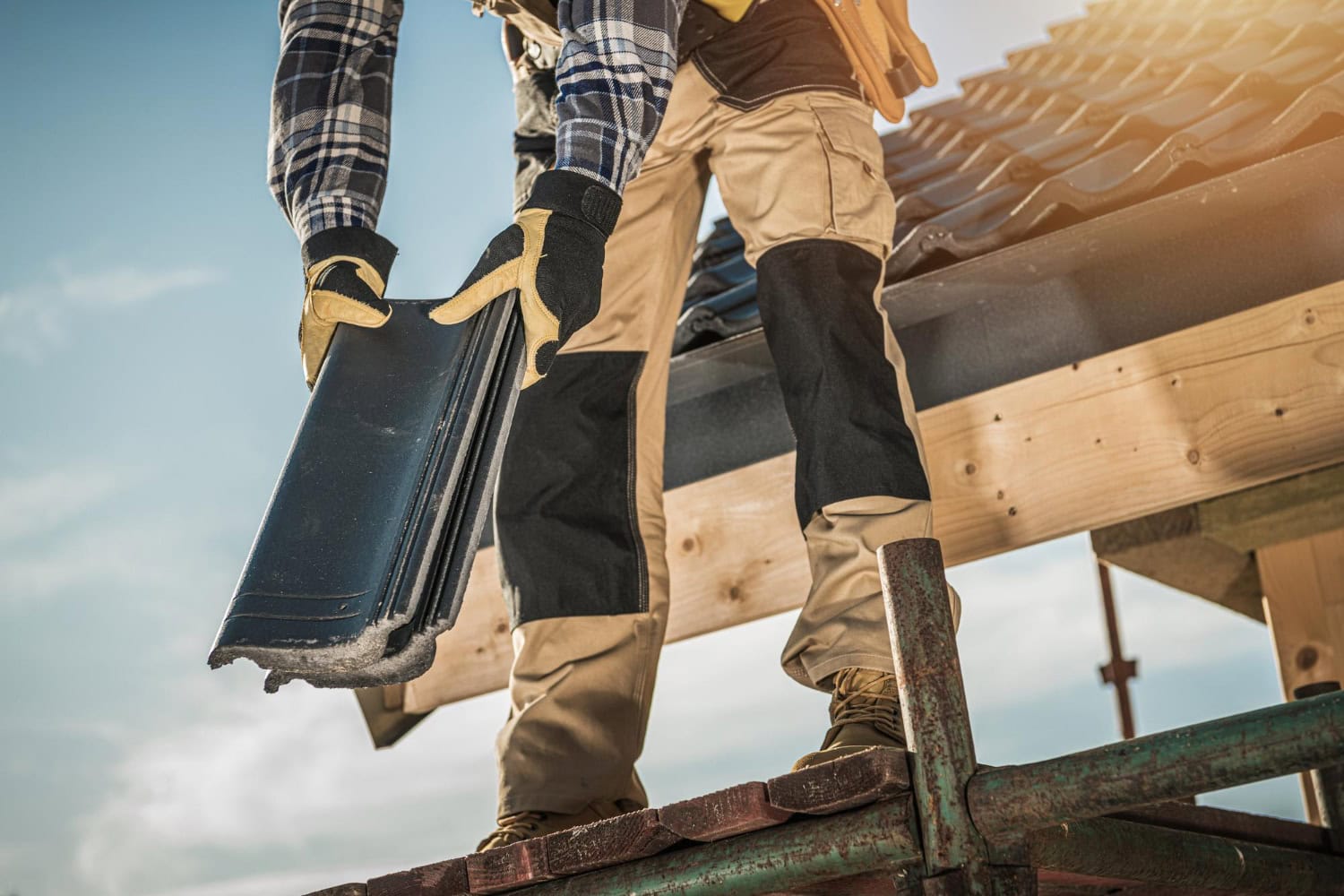 Close-up of a construction worker on scaffolding holding roofing tiles, preparing to install them on a residential roof.