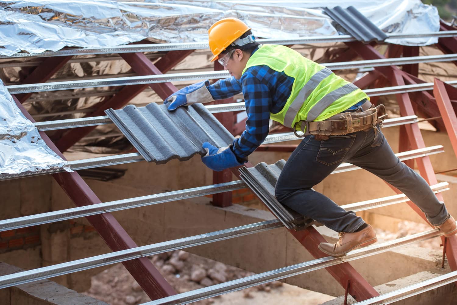 Roofer in safety gear carefully placing a tile onto a metal roof frame structure during a construction project.