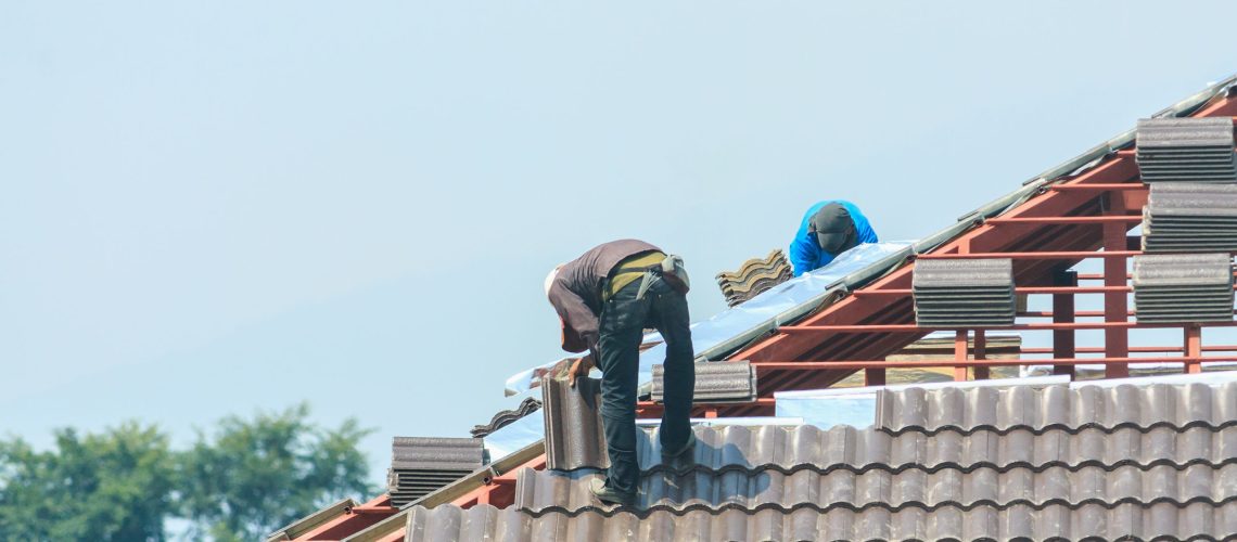 Construction roofer installing roof tiles at house building site