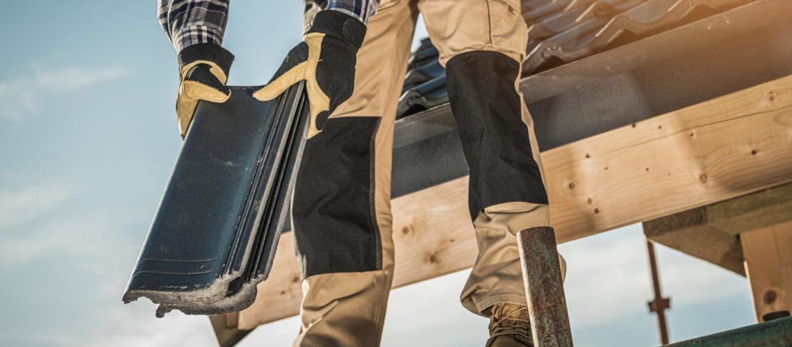 Close-up of a construction worker on scaffolding holding roofing tiles, preparing to install them on a residential roof.